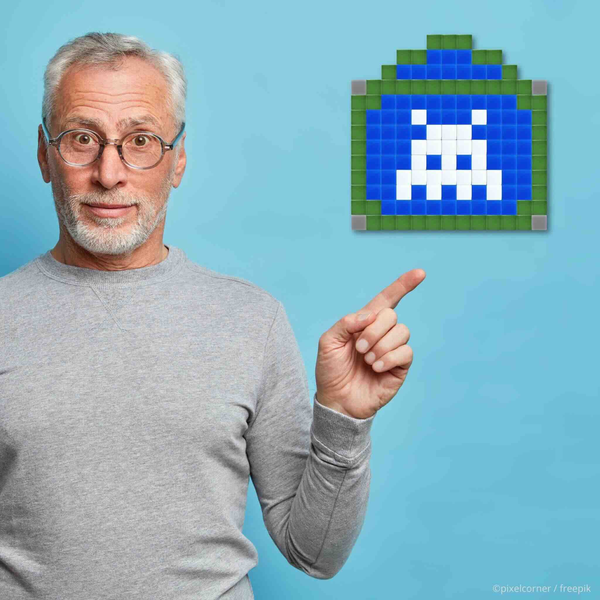 Un homme agé cheveux blanc sur fond bleu montre un kit de pixel art diy en mosaïque de verre accroché en décoration murale representant un alien space invaders