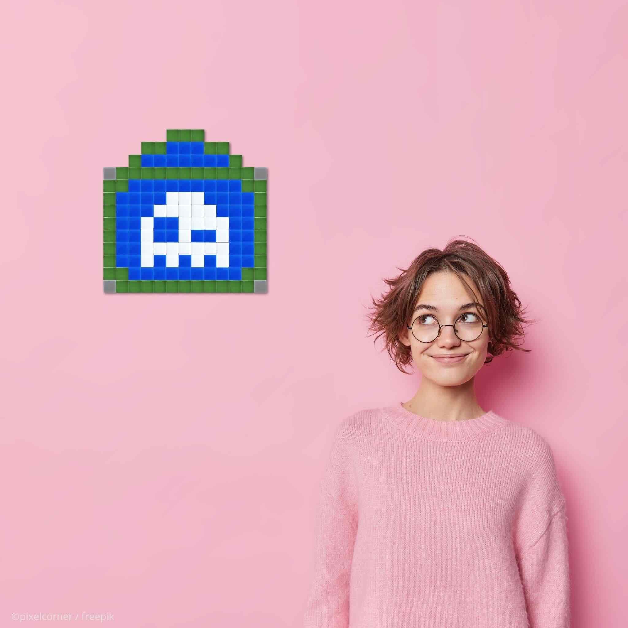 Une fille a lunette à l'air malicieux avec pull rose sur fond rose qui regarde le kit en mosaïque de verre diy representant un fantome qui fait un clin d'oeil en pixel art dans une plaque de rue de paris